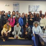 Group of diverse people gathered indoors, posing for a photo in an art-filled setting.