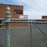 Chain-link fence in foreground with a brick building and "Summit" sign visible behind it.