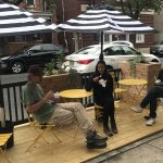 People dining outdoors at a cafe with striped umbrellas and wooden seating.