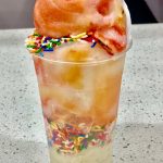 Rainbow sherbet topped colorful ice cream drink in a clear plastic cup.