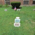 Historic gravestones in a grassy cemetery against a brick building.