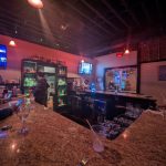 Bar interior with granite countertop, glowing liquor shelves, and dim ambient lighting.