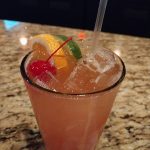 Tropical-themed cocktail with citrus slices and cherry garnish in a glass.