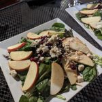 Plated salad with sliced apples, crumbled cheese, and nuts on a white square dish.