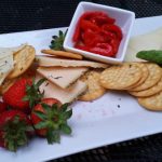 Cheese, crackers, tomatoes, and avocado platter on a white serving dish.