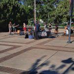 Outdoor music event with a band performing on a paved plaza under a blue sky.
