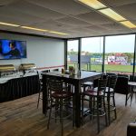 Bar area with TVs and counter, overlooking a baseball field through large windows.