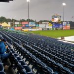 Empty stadium seating rows facing a baseball field under an overcast sky.
