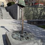 WWI helmet sculpture on a stone pedestal outdoors with steps and trees in background.