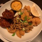 Fried seafood platter with golden-brown pieces and a side of orange dipping sauce.