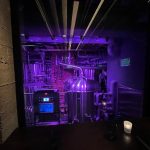 Industrial brewing equipment illuminated with purple light in a dark setting.
