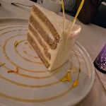 Slice of layered cake with white frosting and gold drizzle on a plate.