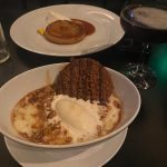 Dessert featuring a stack of waffles, whipped cream, and caramel sauce with a glass of dark beverage.