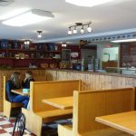 Cafe interior with wooden booths, counter, and patrons seated at tables.