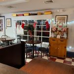 Cafe interior with dining tables, window display featuring holiday decor, and wooden counter.