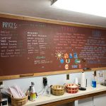 Chalkboard menu displaying prices and toppings for milkshakes, sundaes, and more at a counter.