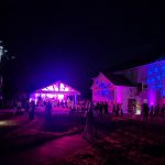 Nighttime outdoor party with illuminated tent and building facade featuring blue star patterns.