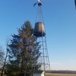 Wind pump tower against a clear blue sky in an open field.