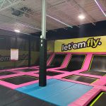 Indoor trampoline park with pink and black trampolines under a high ceiling.