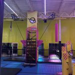 Indoor climbing gym with a large, colorful obstacle course structure under bright lighting.