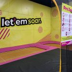 Indoor trampoline park with "let'em soar" branding and a large black jumping surface.