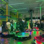 Arcade hall with colorful spinning rides and neon lights in a large indoor space.