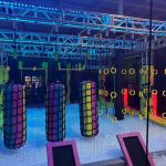 Indoor neon-lit obstacle course with colorful climbing structures and blue lighting.