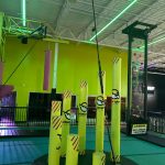 Bright green indoor trampoline park with colorful inflatable pillars and high ceilings.