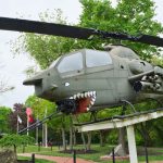 Military helicopter replica with shark mouth displayed outdoors in a park setting.