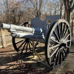 Antique cannon on wooden wheels displayed outdoors in a park setting.