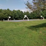 Outdoor sports court with basketball hoops set against a backdrop of green trees and grass.