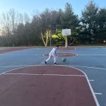 Young boy dribbles a soccer ball on an outdoor basketball court under blue sky.