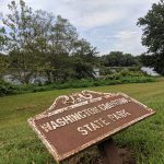 Washington Crossing State Park sign in a grassy area with trees and water in the background.