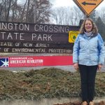 Woman stands in front of Washington Crossing State Park entrance sign.