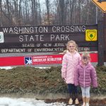 Two young girls stand in front of the Washington Crossing State Park sign.