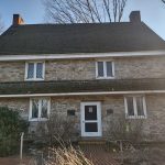 Stone farmhouse with dark roof and white trim, set against a backdrop of bare trees.
