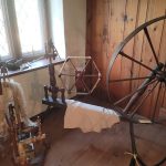 Antique wooden spinning wheel and loom parts in a rustic workshop setting.