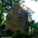 Stone house nestled among lush green trees under a bright sky.