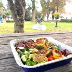 Roasted vegetables in a foil tray on an outdoor wooden picnic table.