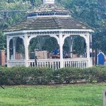 White gazebo with thatched roof in a grassy backyard setting.