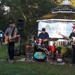 Musicians perform outdoors near a gazebo at Morris Hall during a daytime event.
