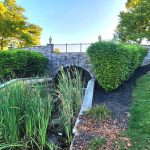 Stone bridge over a small stream with lush green landscaping and trees.