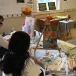 Art class in progress with students painting and working on projects at tables.