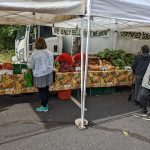 Farmer's market stall with produce under white tents; woman shopping.