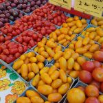 Assortment of fresh tomatoes and yellow peppers displayed in market crates.