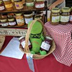 Assortment of homemade pickles and jars displayed at a market stall with a green pickle toy.