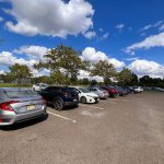 Parked cars in a large outdoor lot under a bright, partly cloudy blue sky.