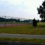 Outdoor sports field with a chain-link fence, running track, and grassy area under a bright sky.