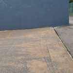 Large, dark gray wall against a paved outdoor area with trees in the background.