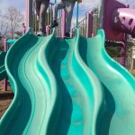 Two boys on playground equipment overlooking a bright blue, wavy slide.